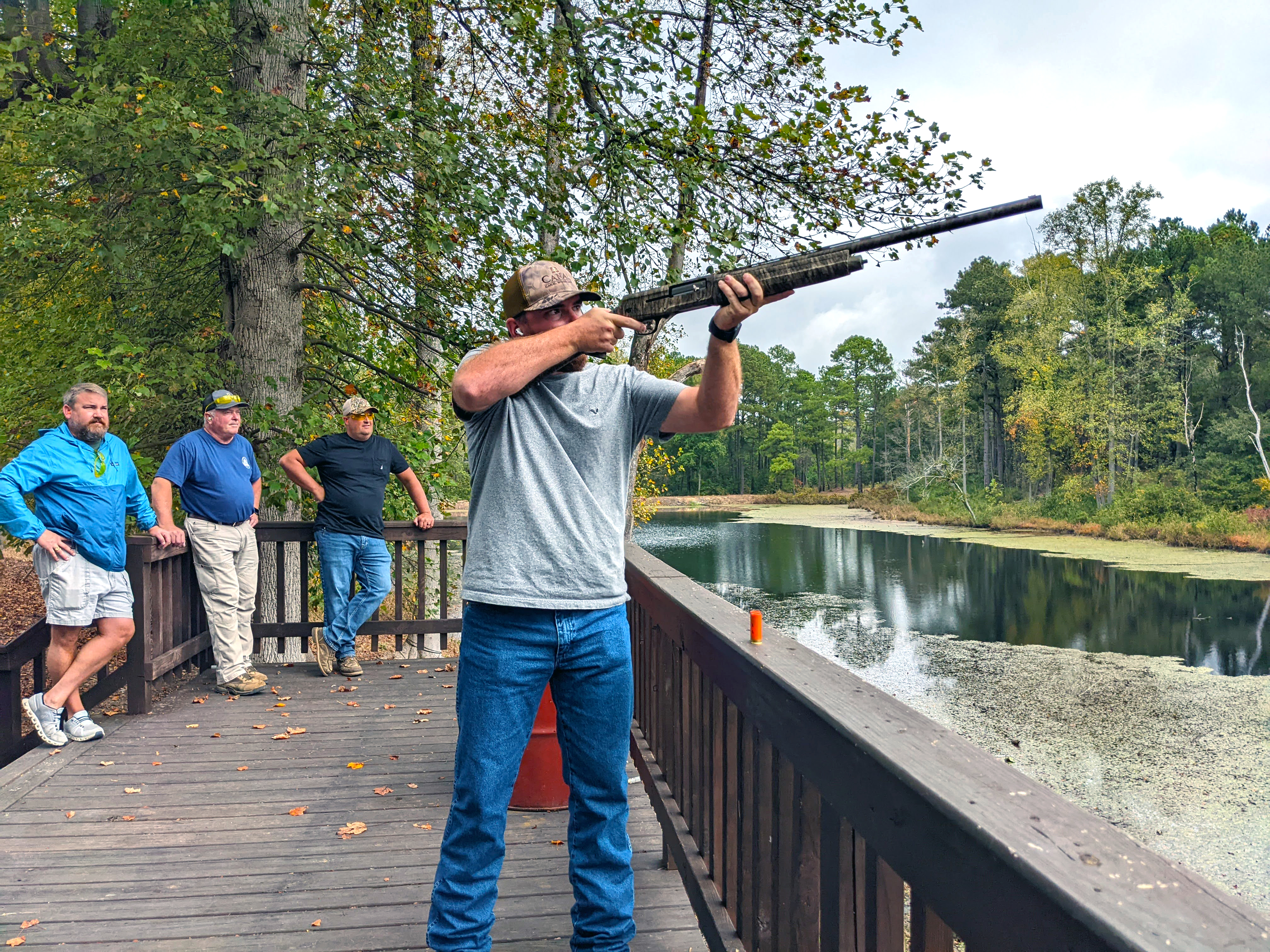 Clay shoot participants aims his shotgun over the pond